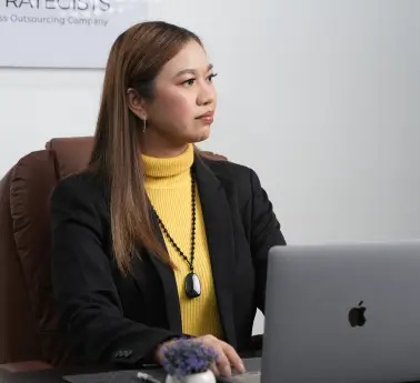 A woman sitting at a desk with a laptop open in front of her, surrounded by an office environment.